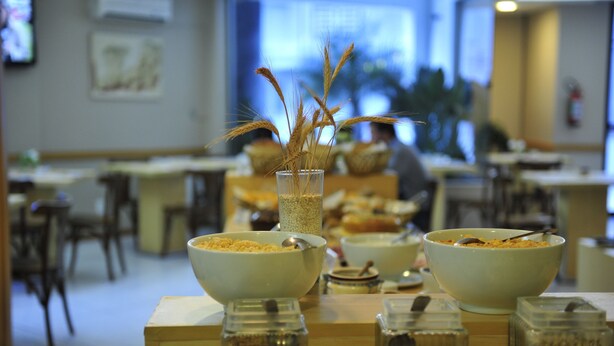 A dining area with tables, chairs, and a buffet setup with bowls and containers. - Bergson Flat (Caxias do Sul)