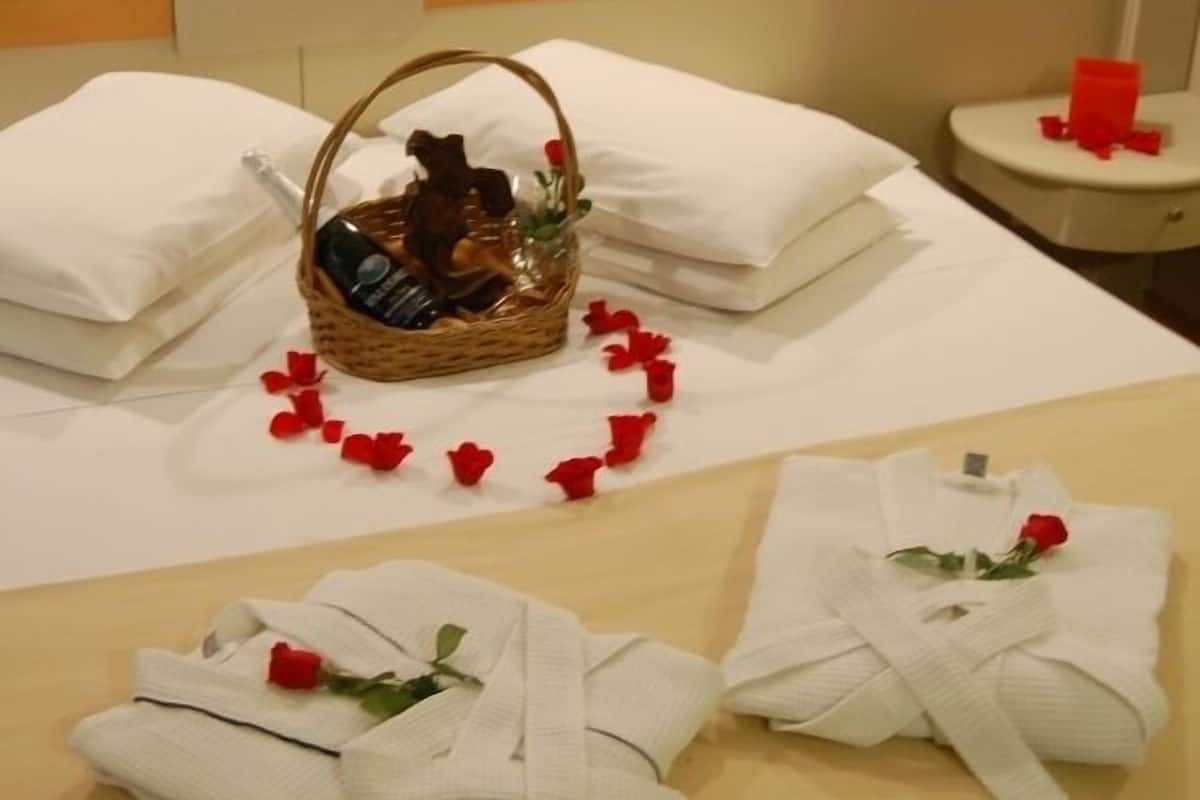 Un lit bien fait, avec du linge de lit blanc, un panier contenant des articles de toilette et une composition florale de pétales de rose.