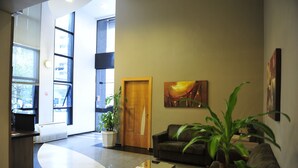 A modern lobby with a reception desk, a wooden door, a couch, and a large window with blinds. - Bergson Flat (Caxias do Sul)