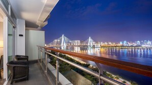 A balcony with wicker furniture, a view of a city skyline, and a bridge at night. - InterContinental Haikou Seaview by IHG (Haikou)