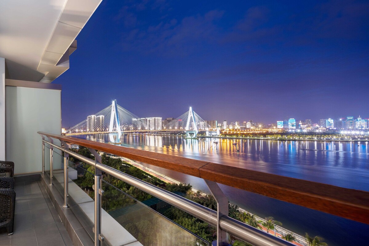 A balcony with wicker furniture, a view of a city skyline, and a bridge at night.