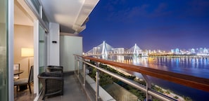 A balcony with wicker furniture, a view of a city skyline, and a bridge at night. - InterContinental Haikou Seaview by IHG (Haikou)