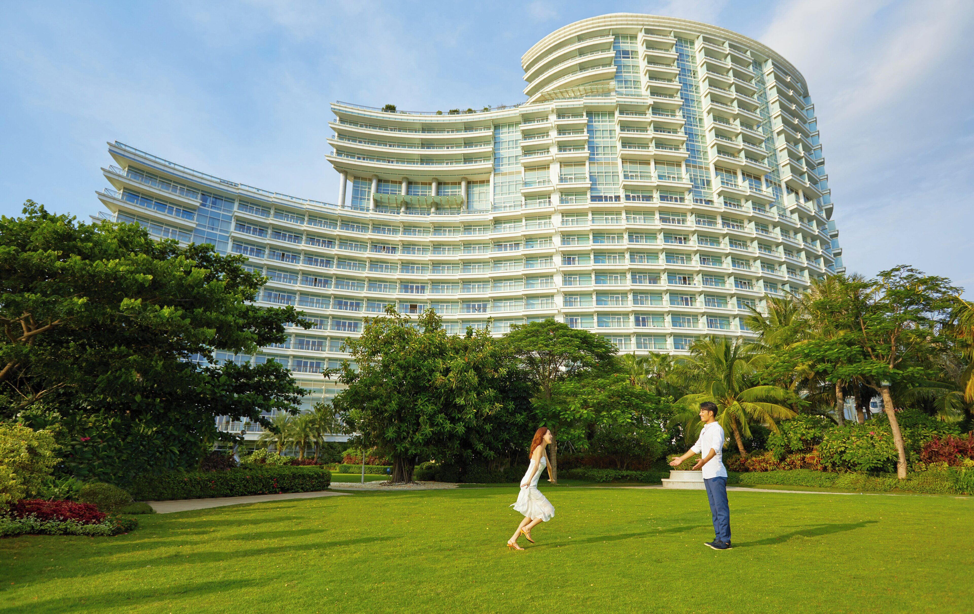 Un hotel moderno con fachada curva, abundante vegetación y césped cuidado.
