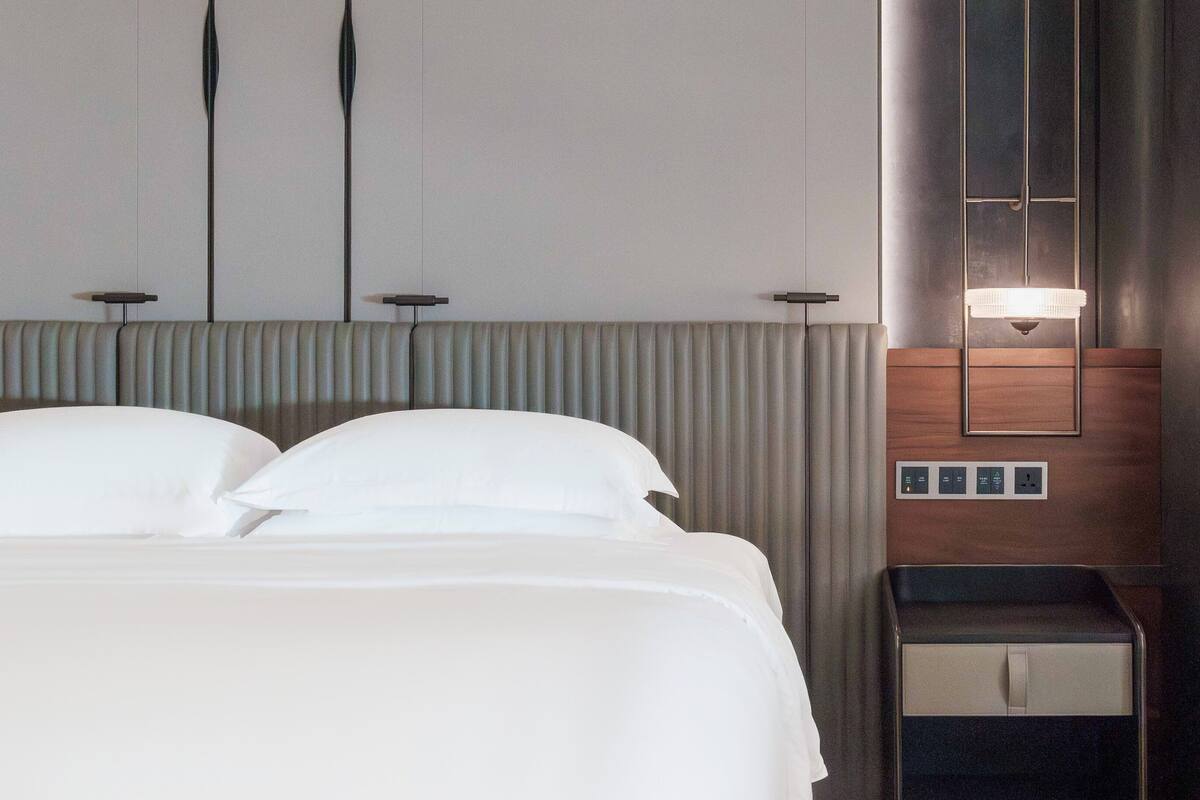 A hotel room with a large bed, a bedside table, a mirror, and a wall-mounted light fixture.