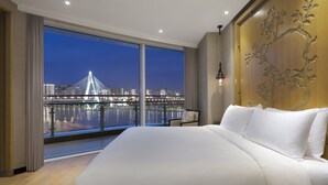 A modern hotel room with a large bed, a view of a cityscape and a bridge at night, and a decorative wall panel. - InterContinental Haikou Seaview by IHG (Haikou)