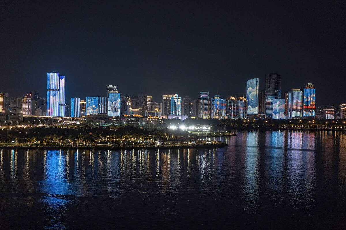 A nighttime cityscape with illuminated skyscrapers reflecting on the water.