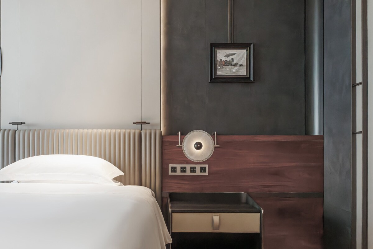 Una habitación de hotel moderna con cama, mesita de noche y una lámpara fijada en la pared.