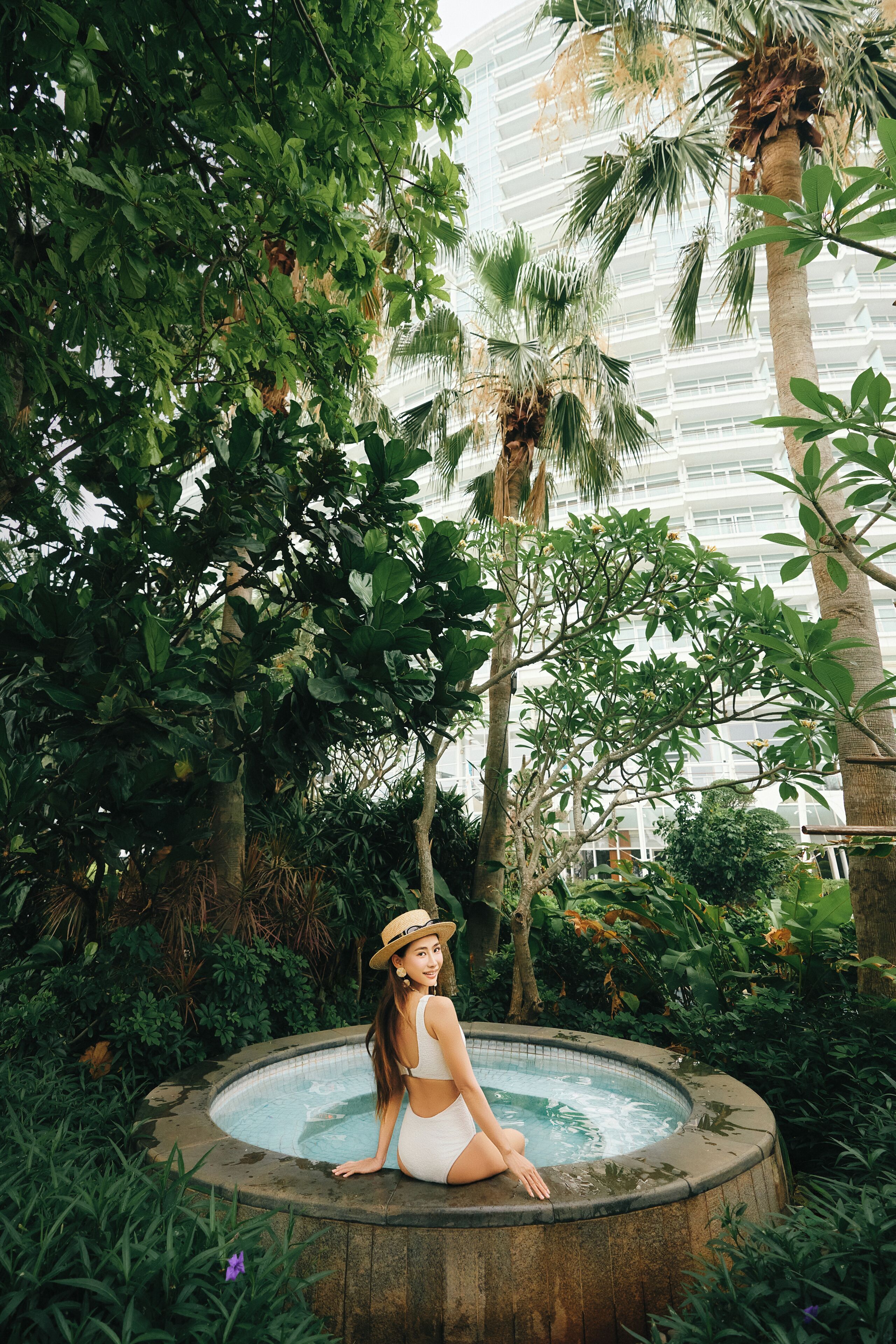 A woman sitting in a hot tub surrounded by lush greenery and tall palm trees.