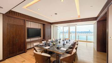 A conference room with a large table, chairs, a flat-screen TV, and a view of a city skyline through large windows.