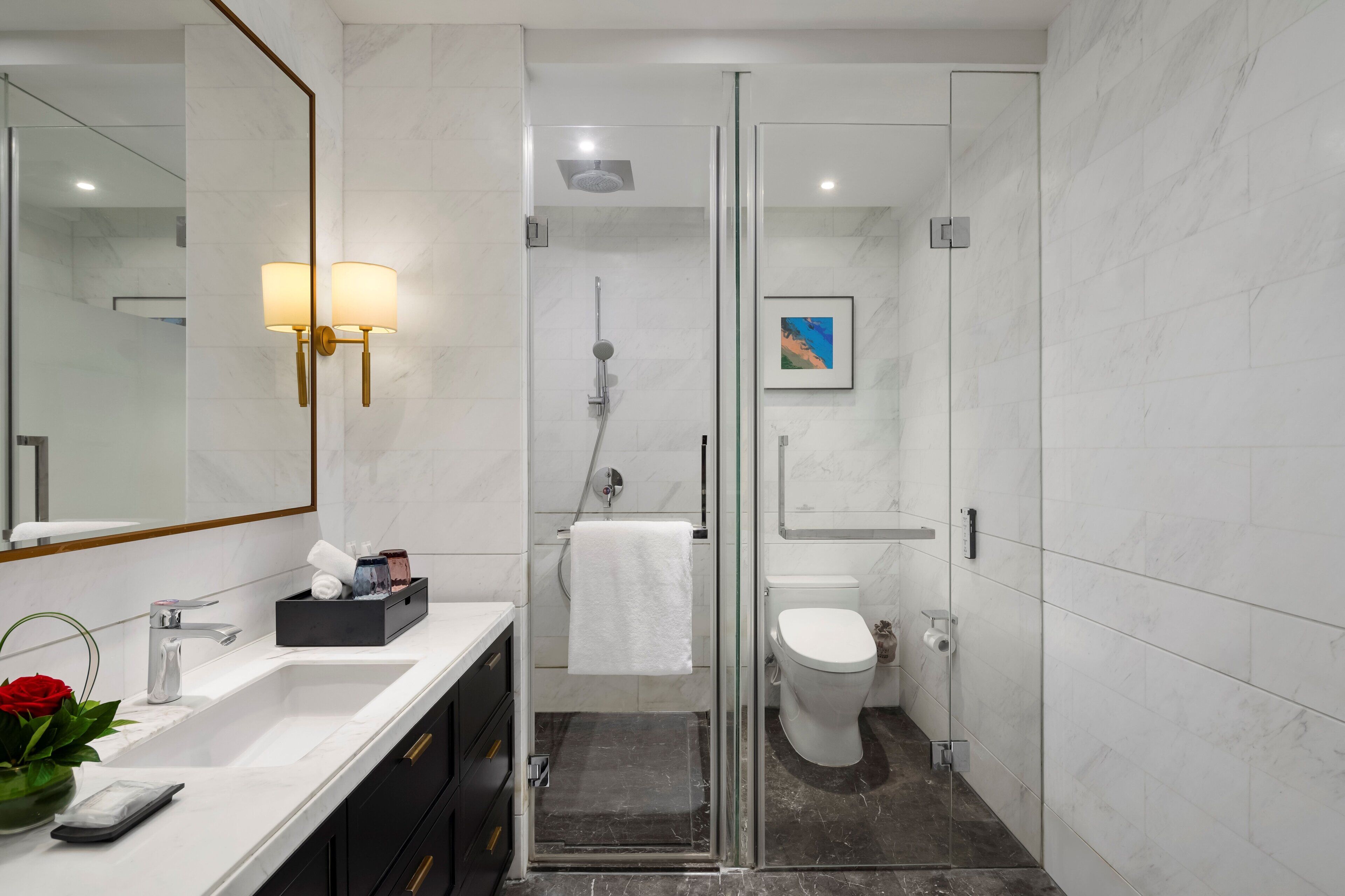 A modern bathroom with a glass-enclosed shower, a white sink with a marble countertop, and a large mirror.
