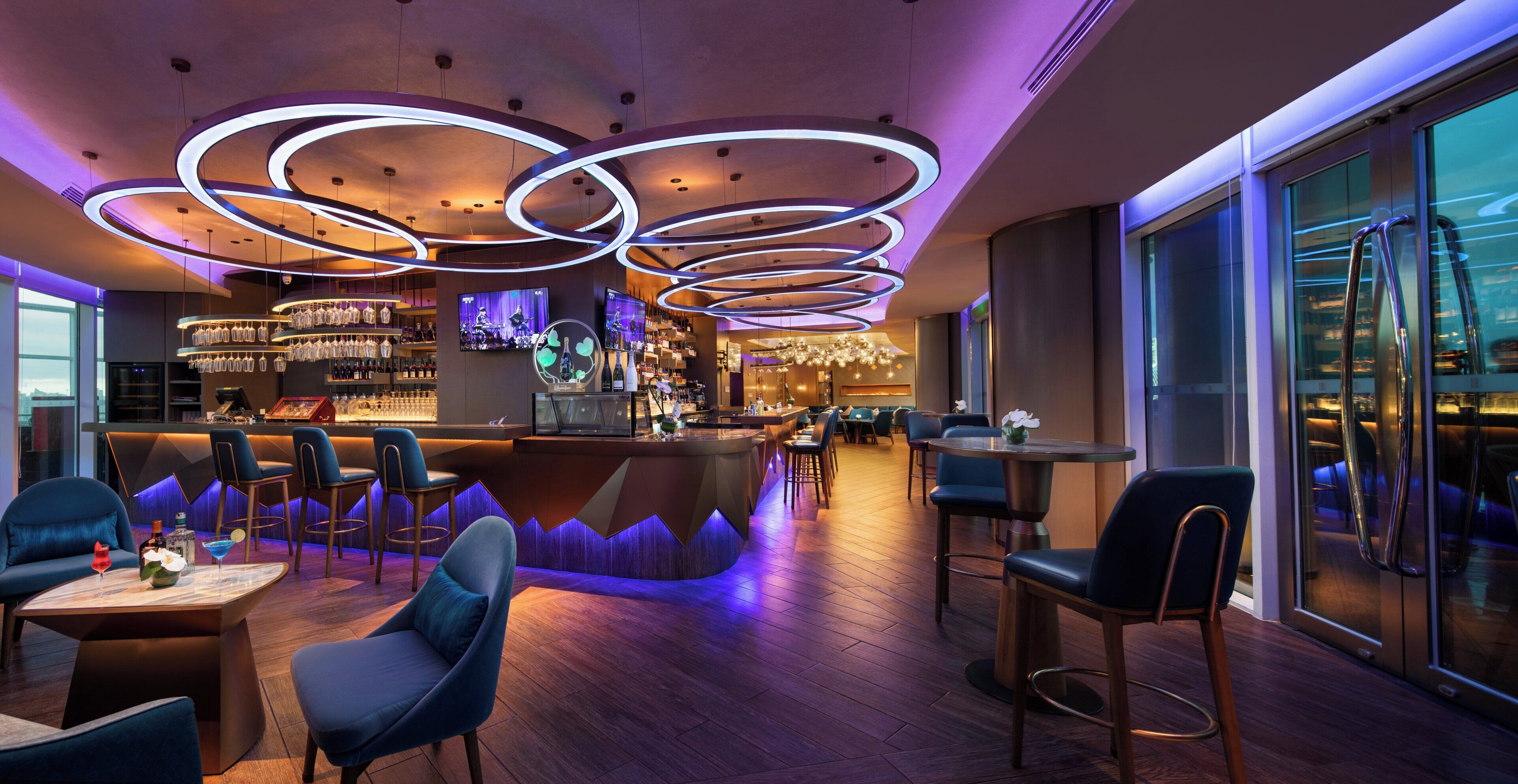 Zona de bar moderna con una barra curva, taburetes y una pantalla de televisión.