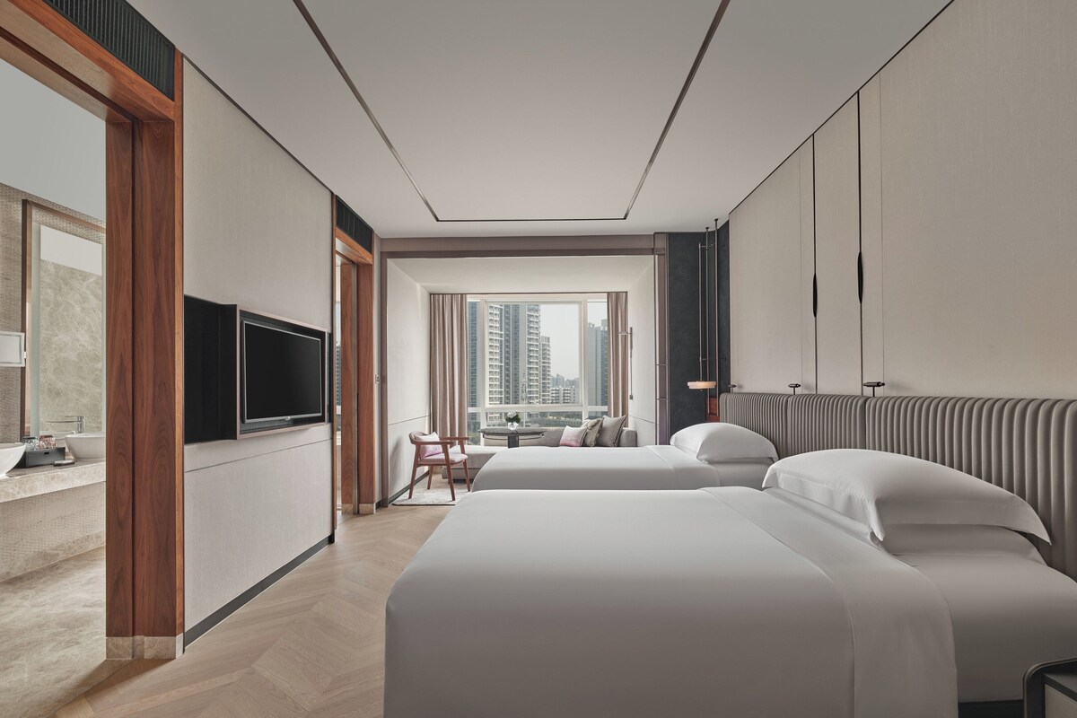 Una habitación de hotel moderna con dos camas, televisión, escritorio y vistas a la ciudad.