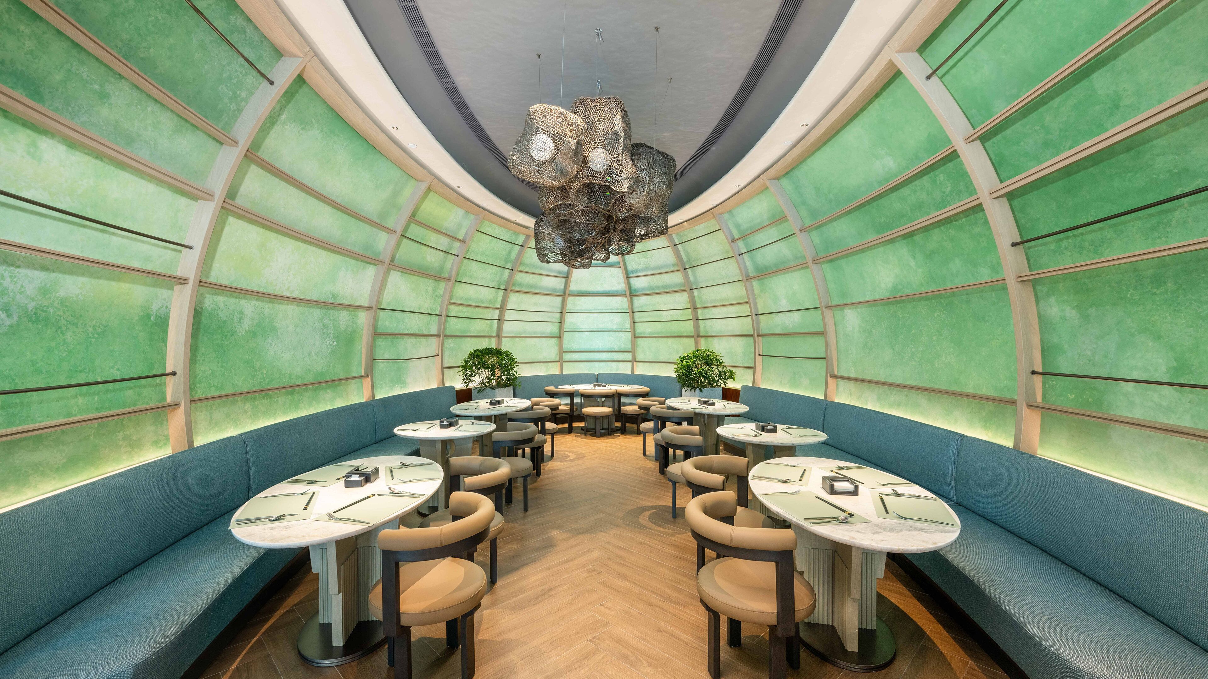 Un intérieur moderne avec un espace salon central, des tables rondes et des murs aux nuances de vert.