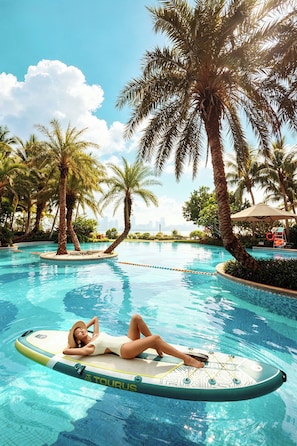 A person lying on a floating board in a pool surrounded by palm trees.