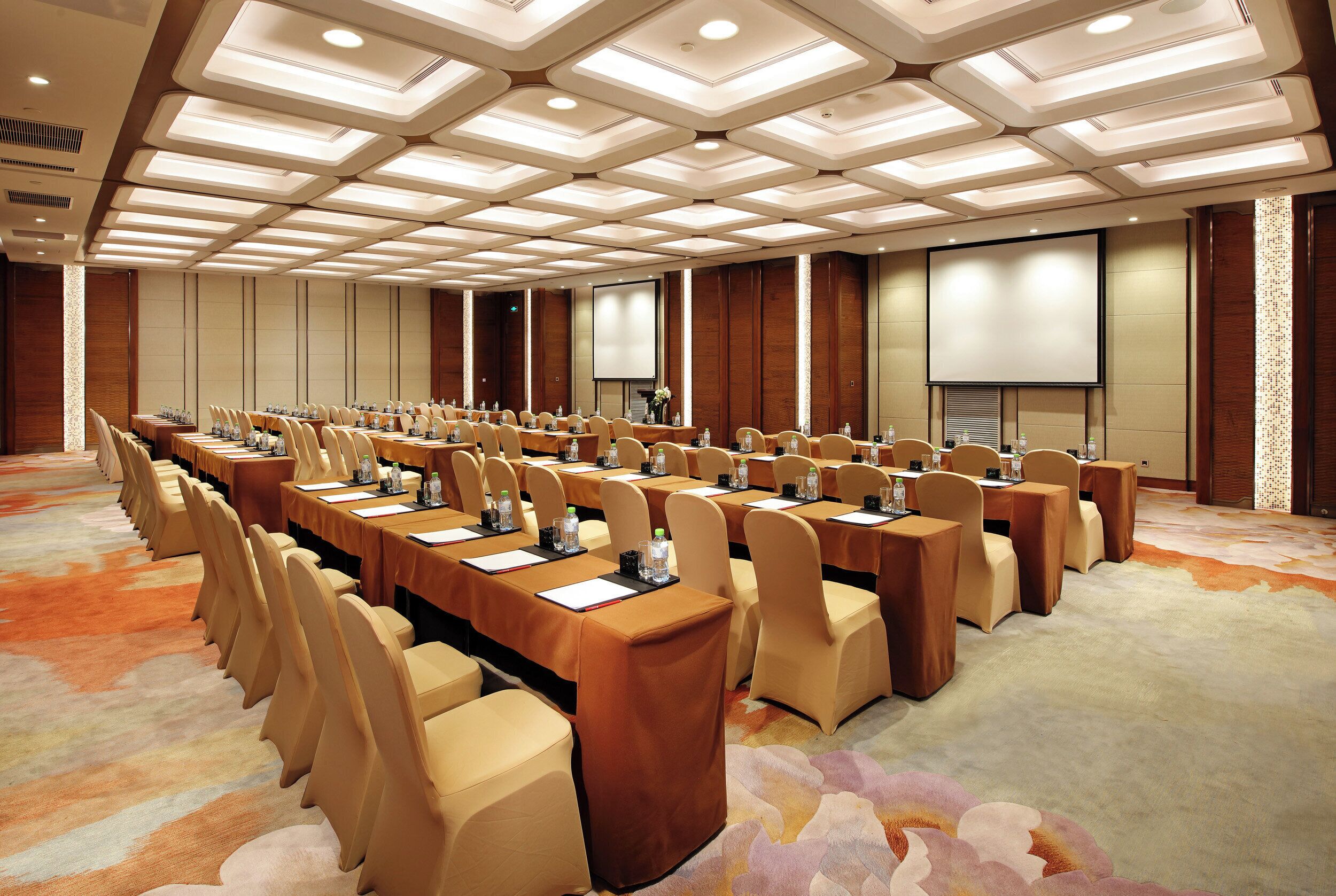 A conference room with multiple tables and chairs, a large screen, and a patterned carpet.
