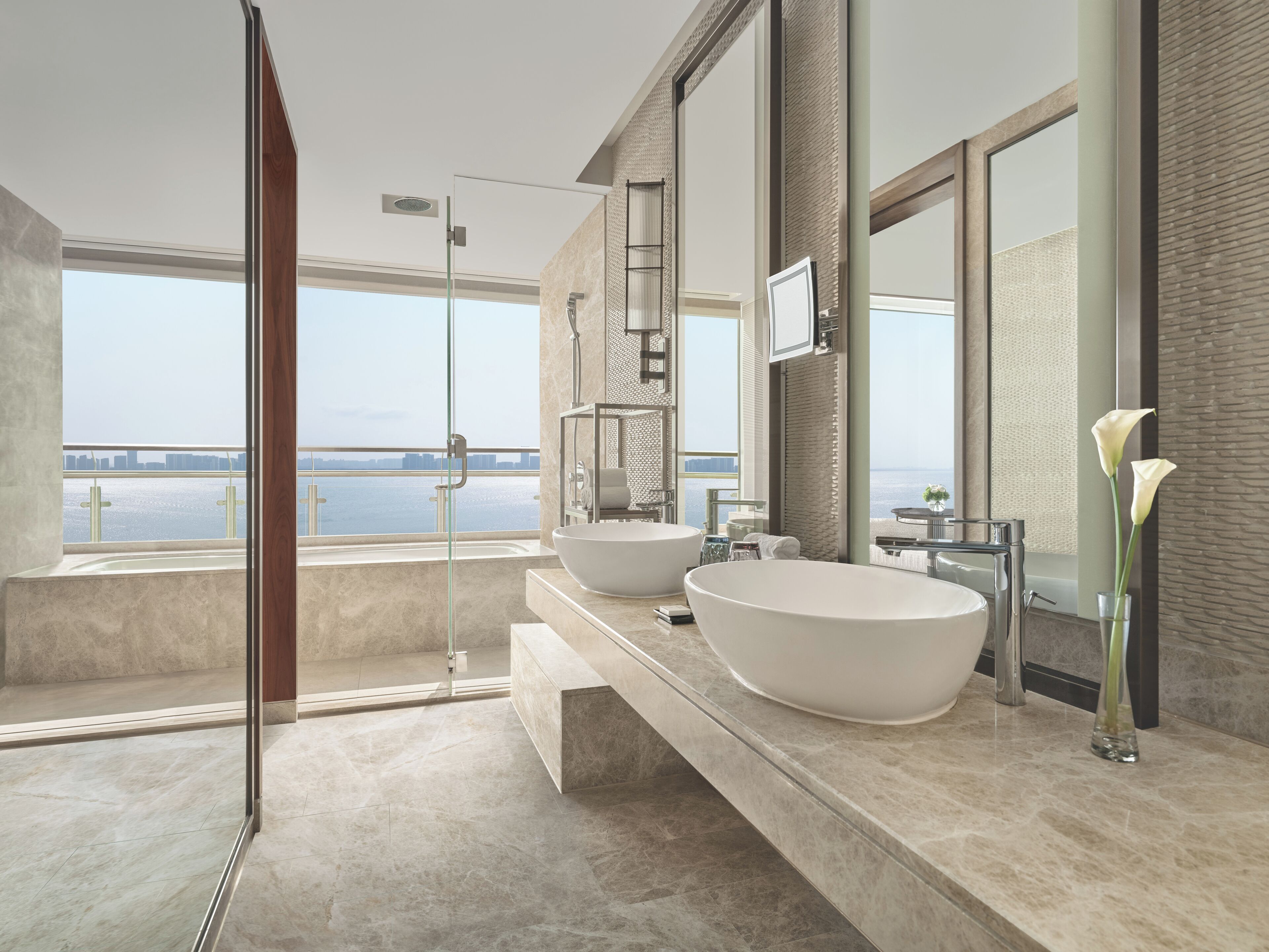 Un baño moderno con dos lavamanos grandes, cabina de ducha de vidrio y vista al agua.