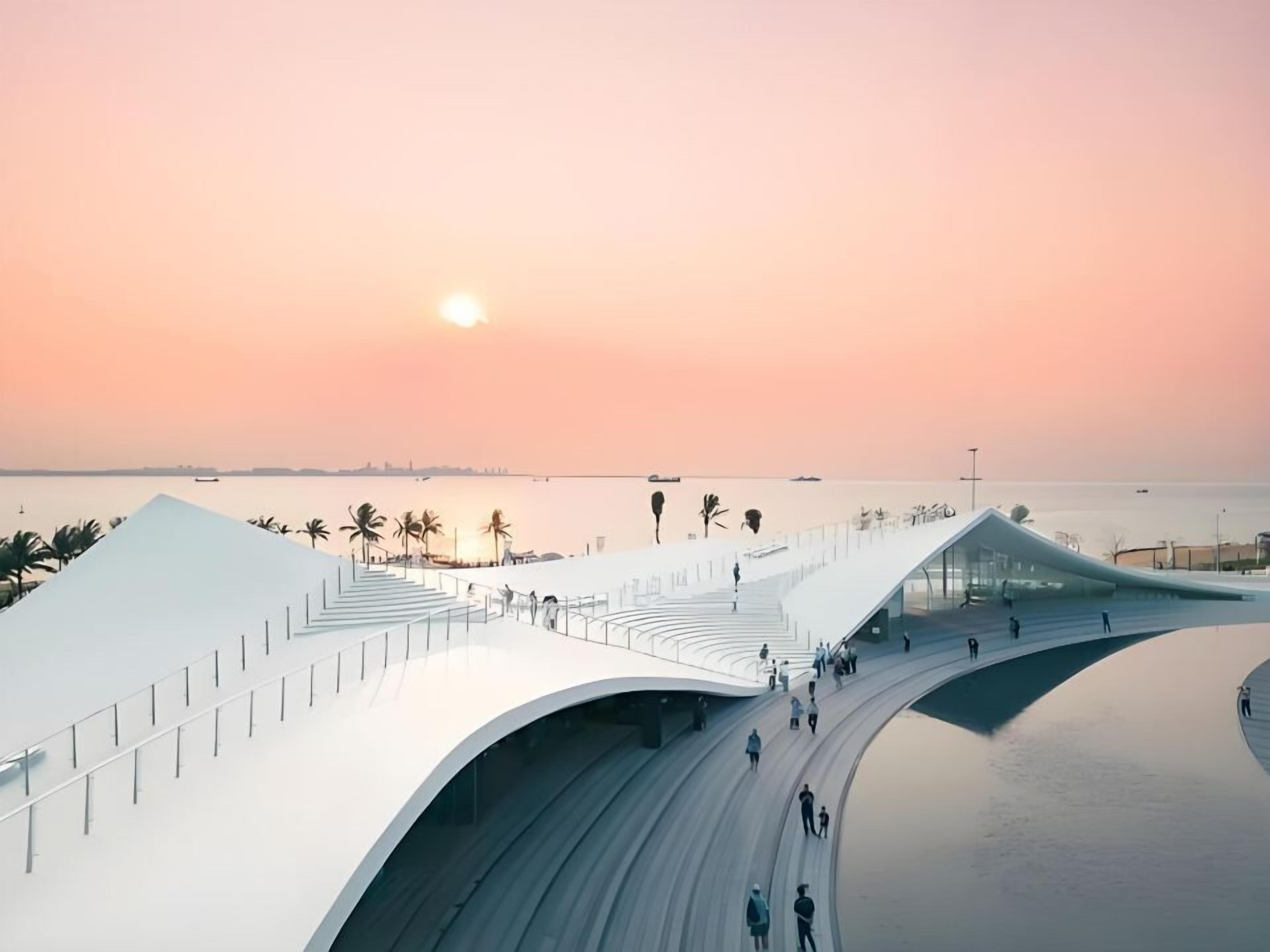 A modern architectural structure with a curved design, a pedestrian walkway, and a view of the sea at sunset.
