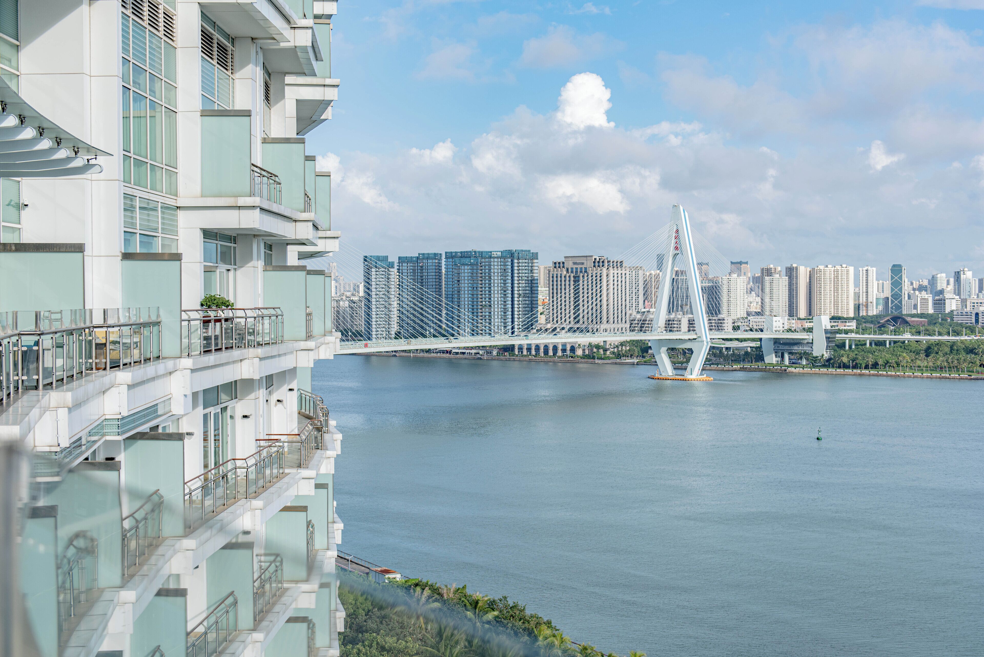 A modern high-rise hotel with balconies overlooking a river and a bridge.