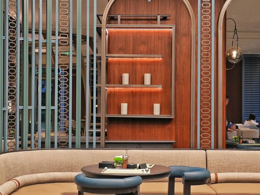 A modern interior with a curved sofa, two chairs, a small table, and a wooden wall with shelves.