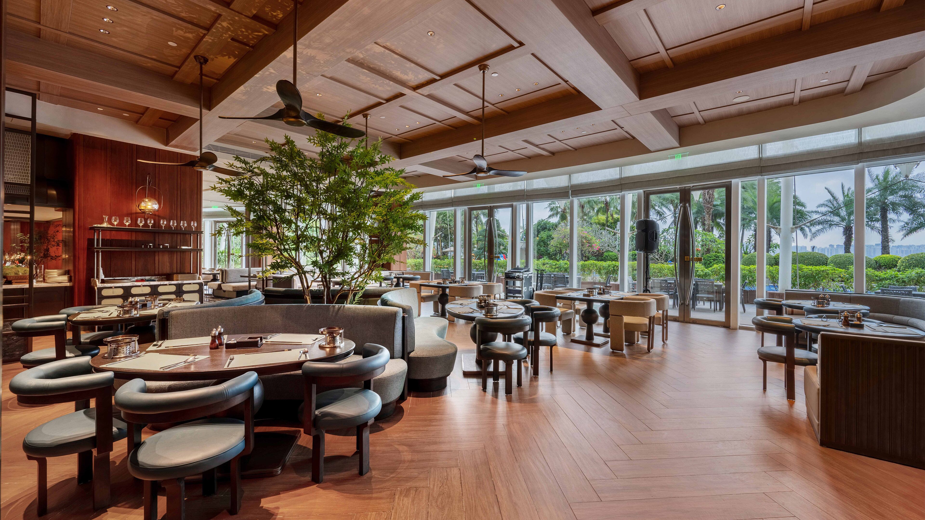 En rymlig restaurang med trägolv och stora fönster som erbjuder utsikt över palmer och stadens silhuett.