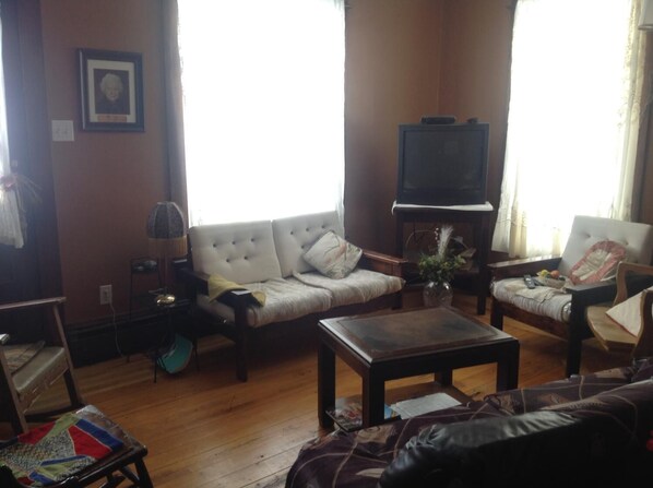 A living room with a sofa, armchairs, a coffee table, a television, and a lamp. - Maison McKenzie House (Campbellton)