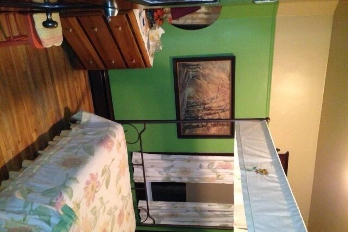 Une petite pièce, de taille modeste, avec un lit superposé, une tête de lit en bois, un mur vert et un tableau encadré.