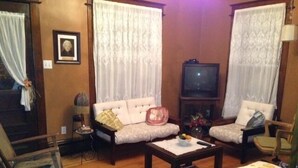 A living room with a sofa, armchairs, a coffee table, a TV, and a wooden floor.