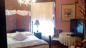 A bedroom with a bed, a desk, a chair, a television, and a chandelier.