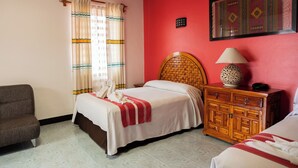 Una habitación de hotel con cama, una mesita de noche de madera, una silla y un aire acondicionado instalado en la pared.
