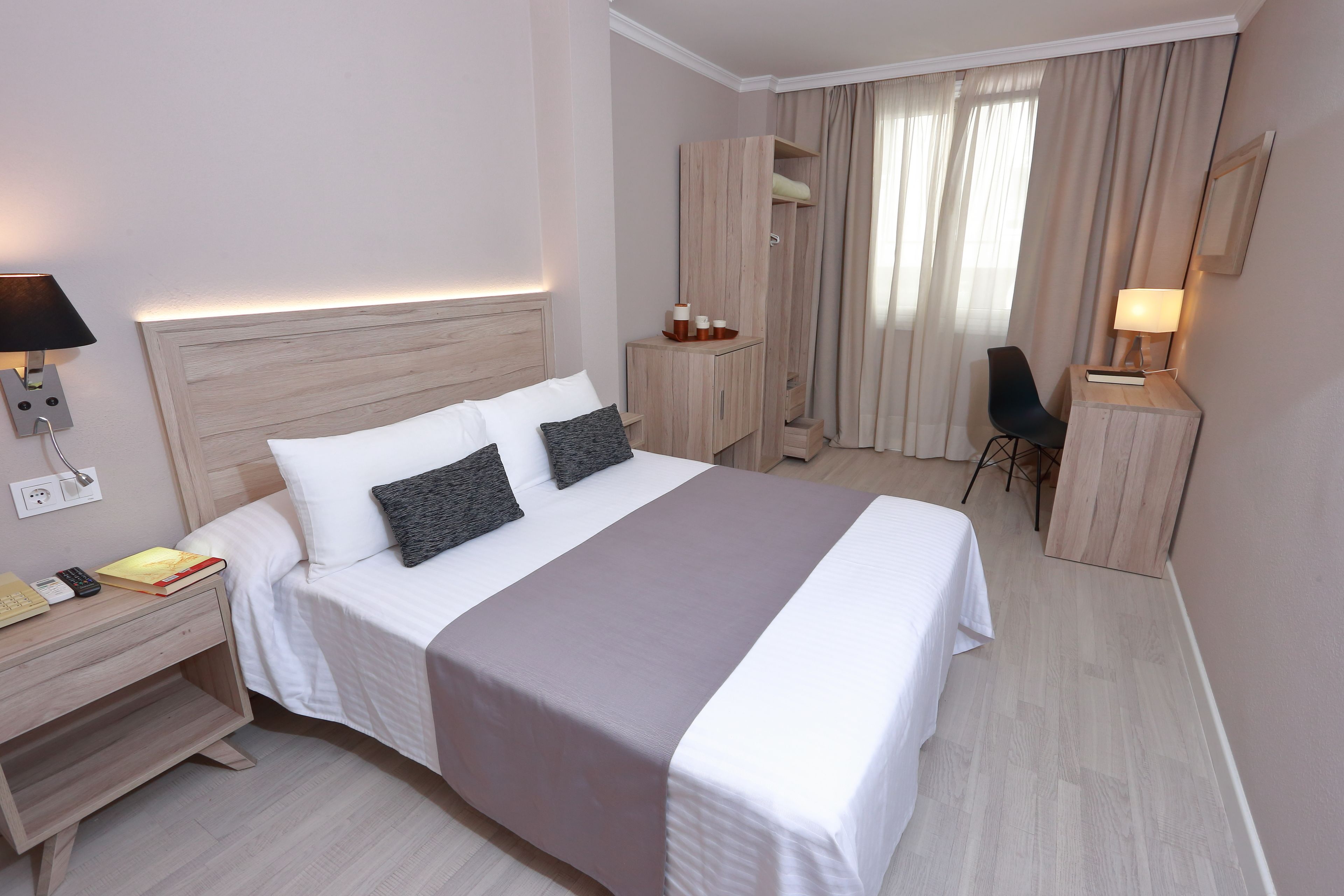 A neatly made bed with a headboard, bedside tables, a desk, and a chair.