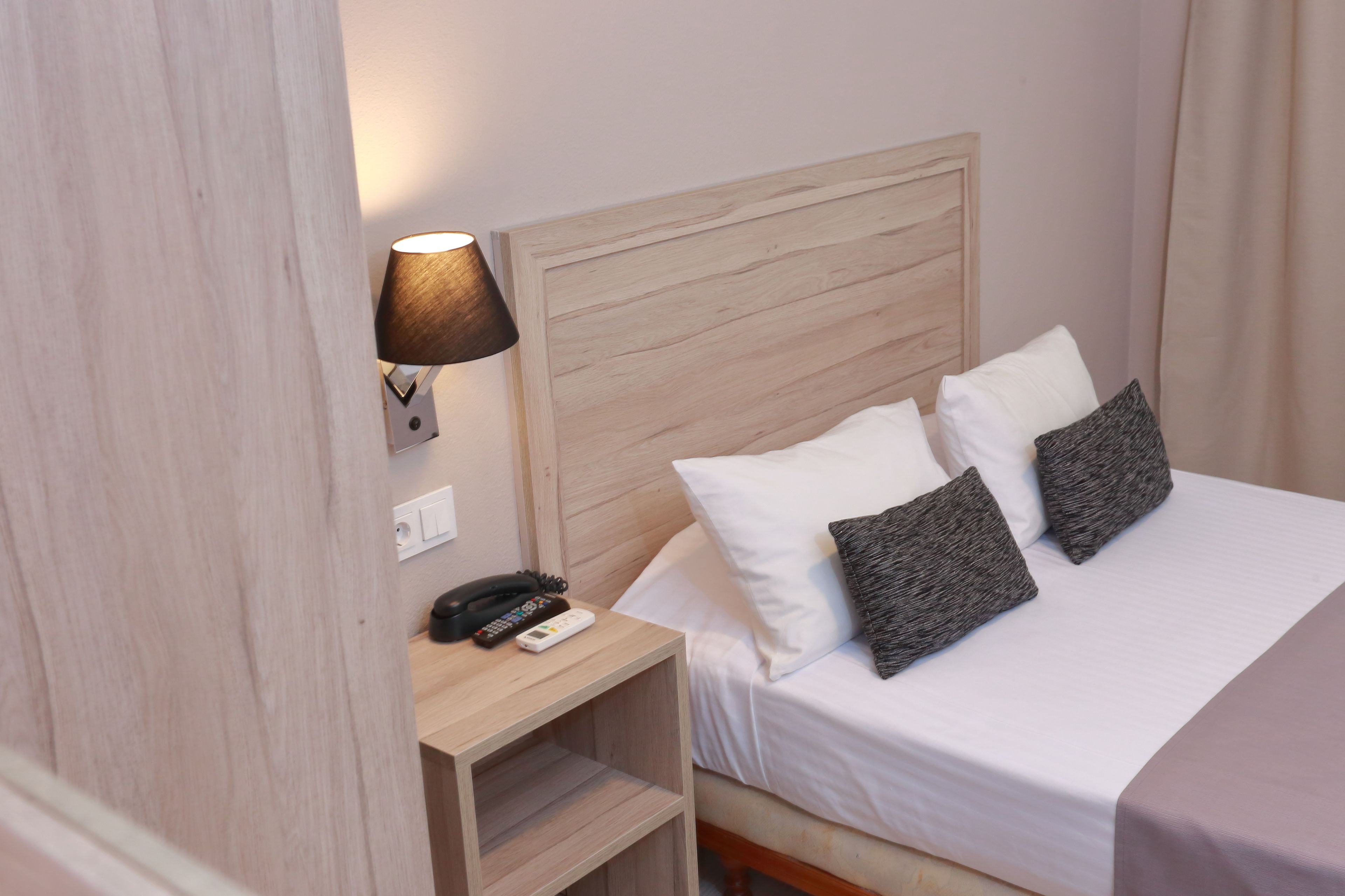 Habitación de hotel con cabecera de madera, mesita de noche con lámpara, teléfono y dos almohadas.