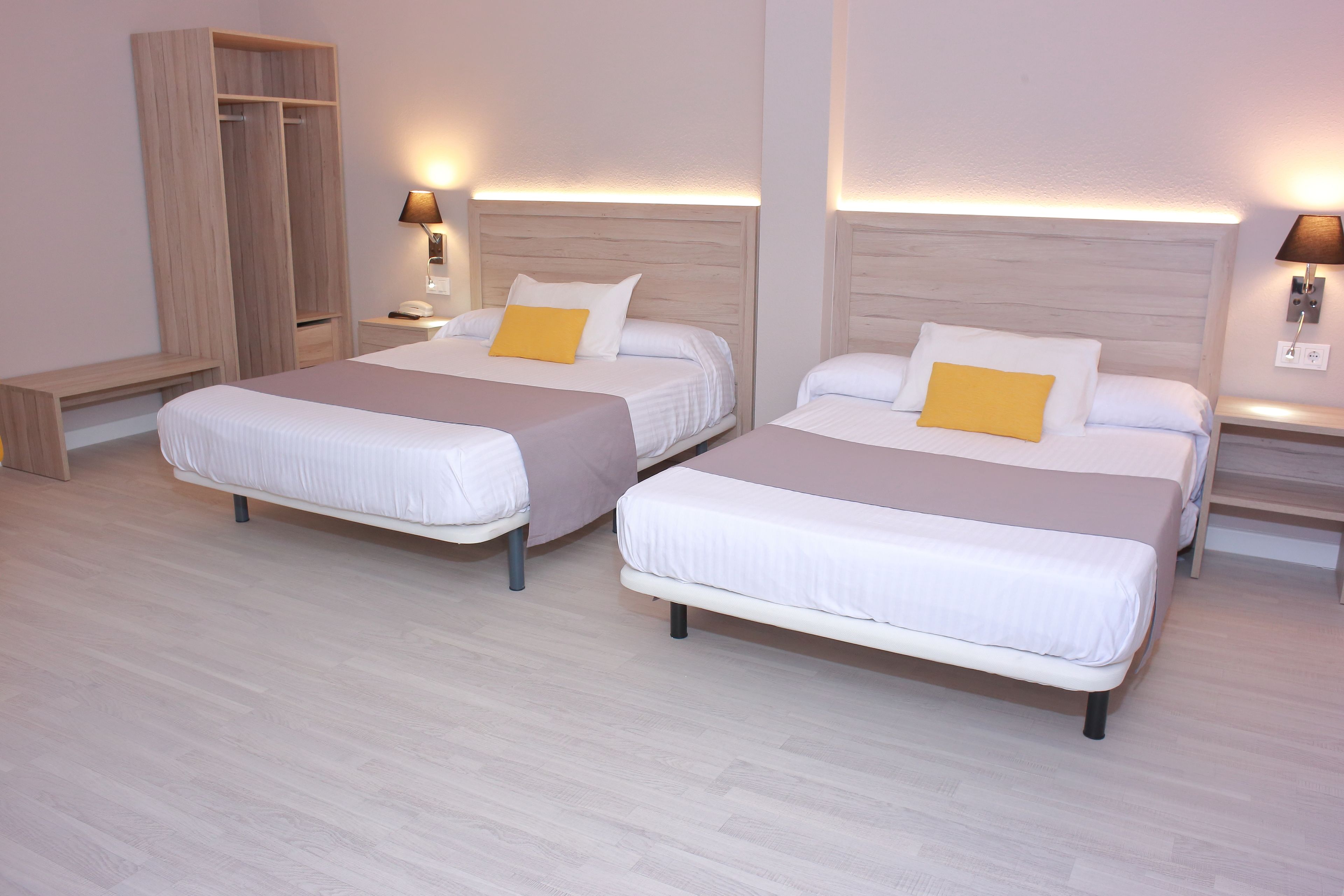 Dos camas individuales con cabeceros de madera, mesitas de noche con lámparas y un armario de madera.