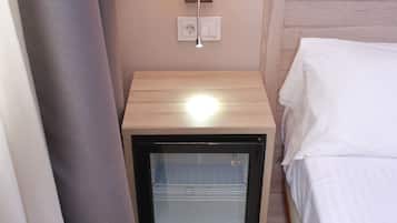 A hotel room with a bed, a bedside table with a lamp, and a minibar.