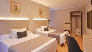 A hotel room with two beds, a desk, a chair, and a wardrobe.