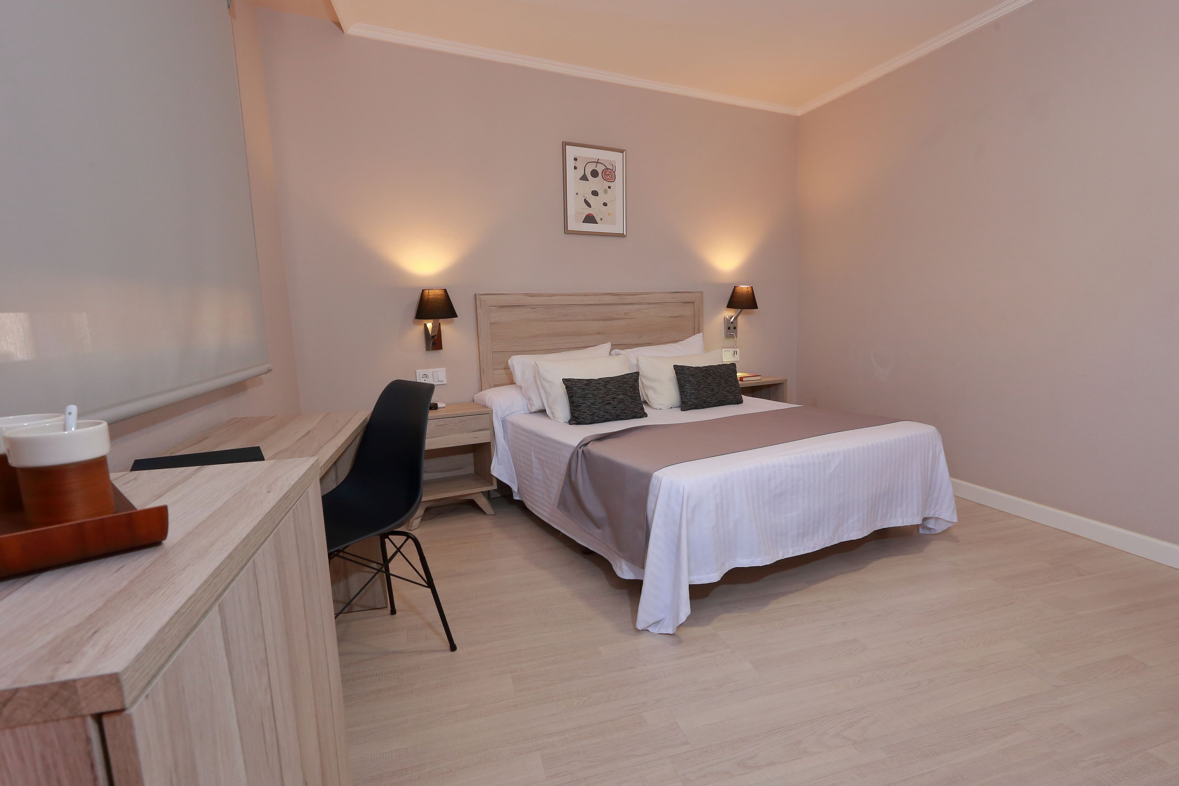 Un dormitorio ordenado con cama, mesitas de noche, escritorio y una silla.
