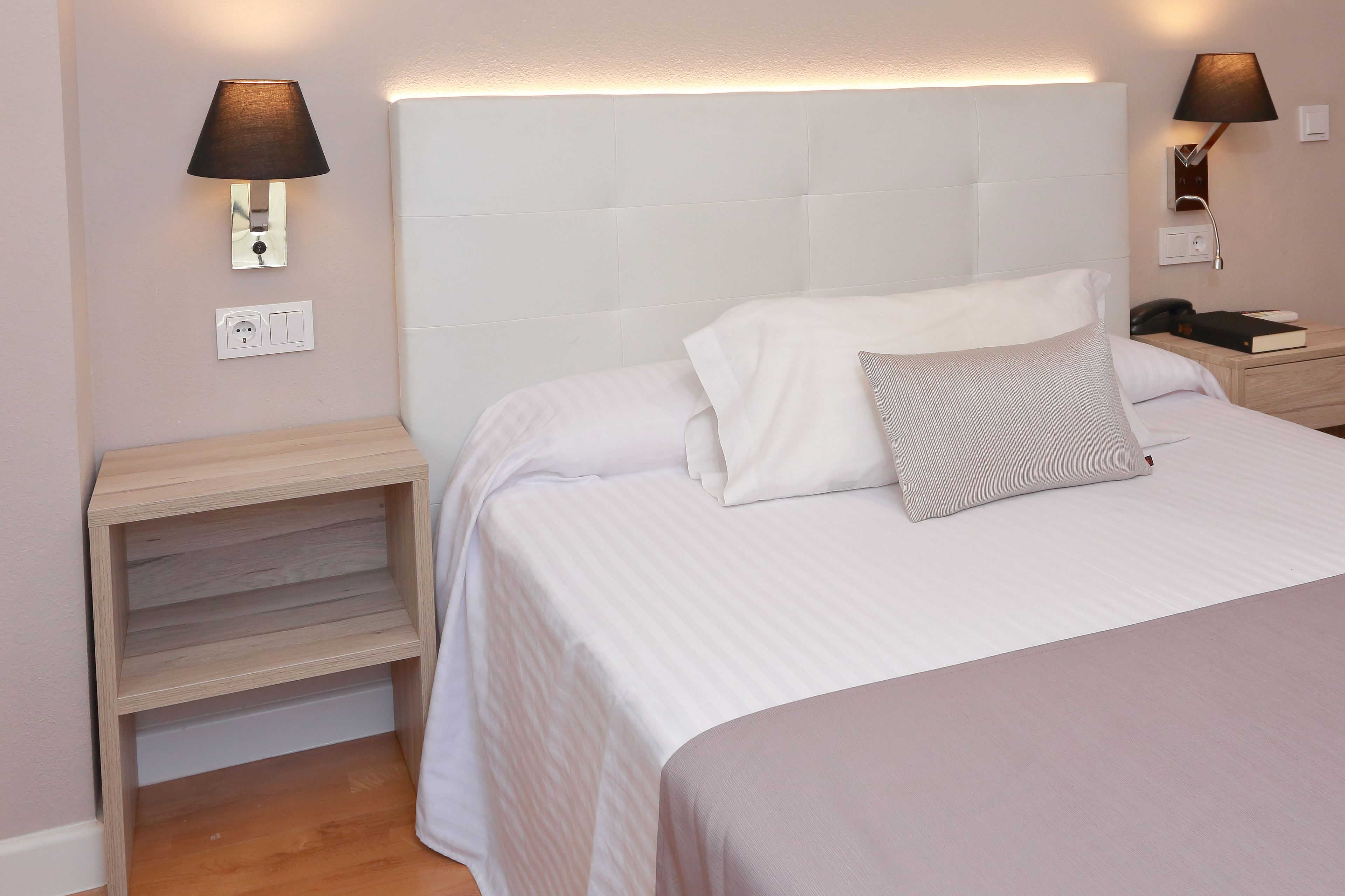 A neatly made bed with white bedding and a single pillow, flanked by two bedside tables with lamps.