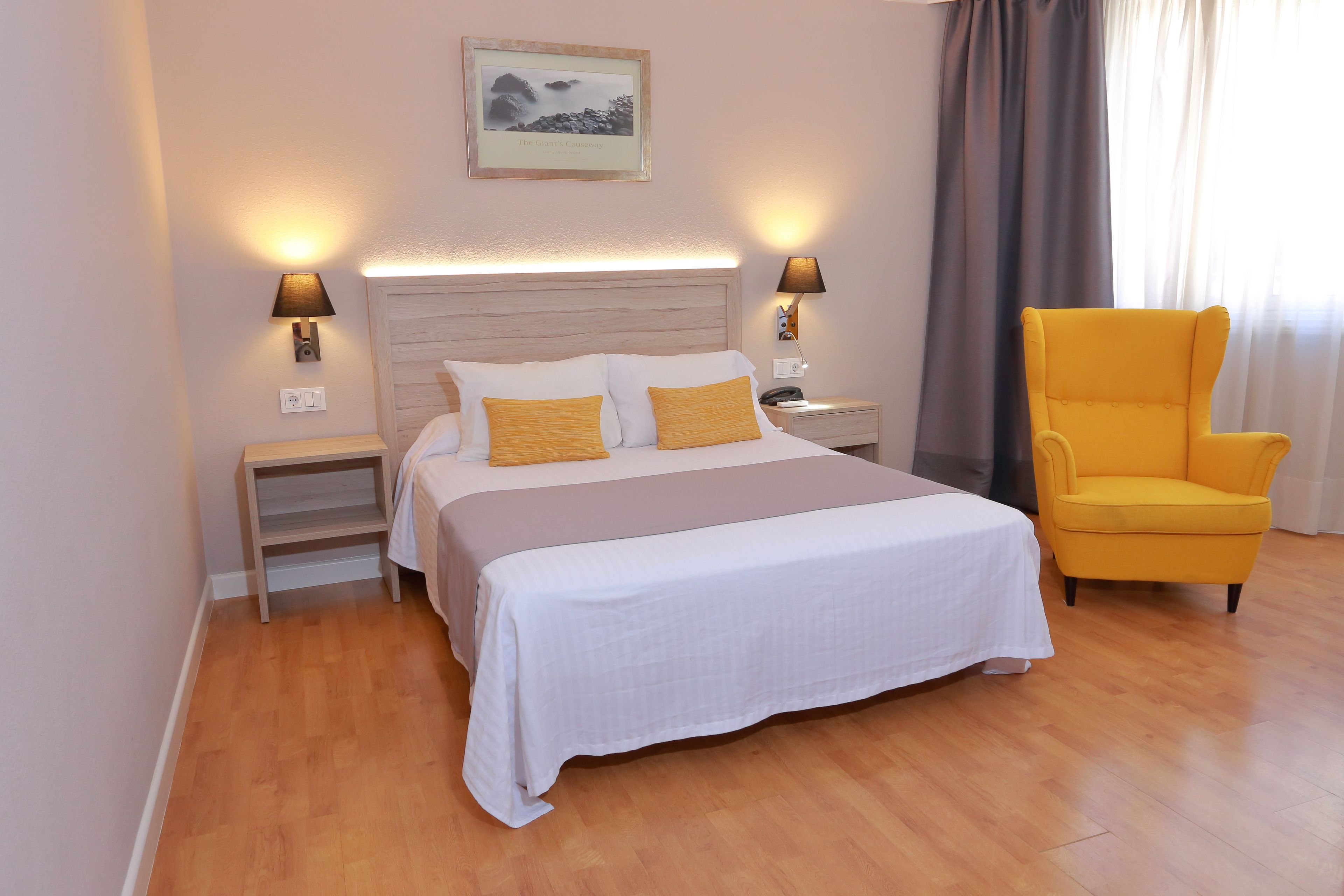 Ein Hotelzimmer mit einem großen Bett, zwei Nachttischlampen, einem Nachttisch, einem Sessel und einem gerahmten Bild an der Wand.