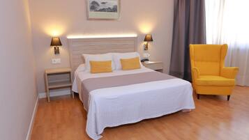 Ein Hotelzimmer mit einem großen Bett, zwei Nachttischlampen, einem Nachttisch, einem Sessel und einem gerahmten Bild an der Wand.