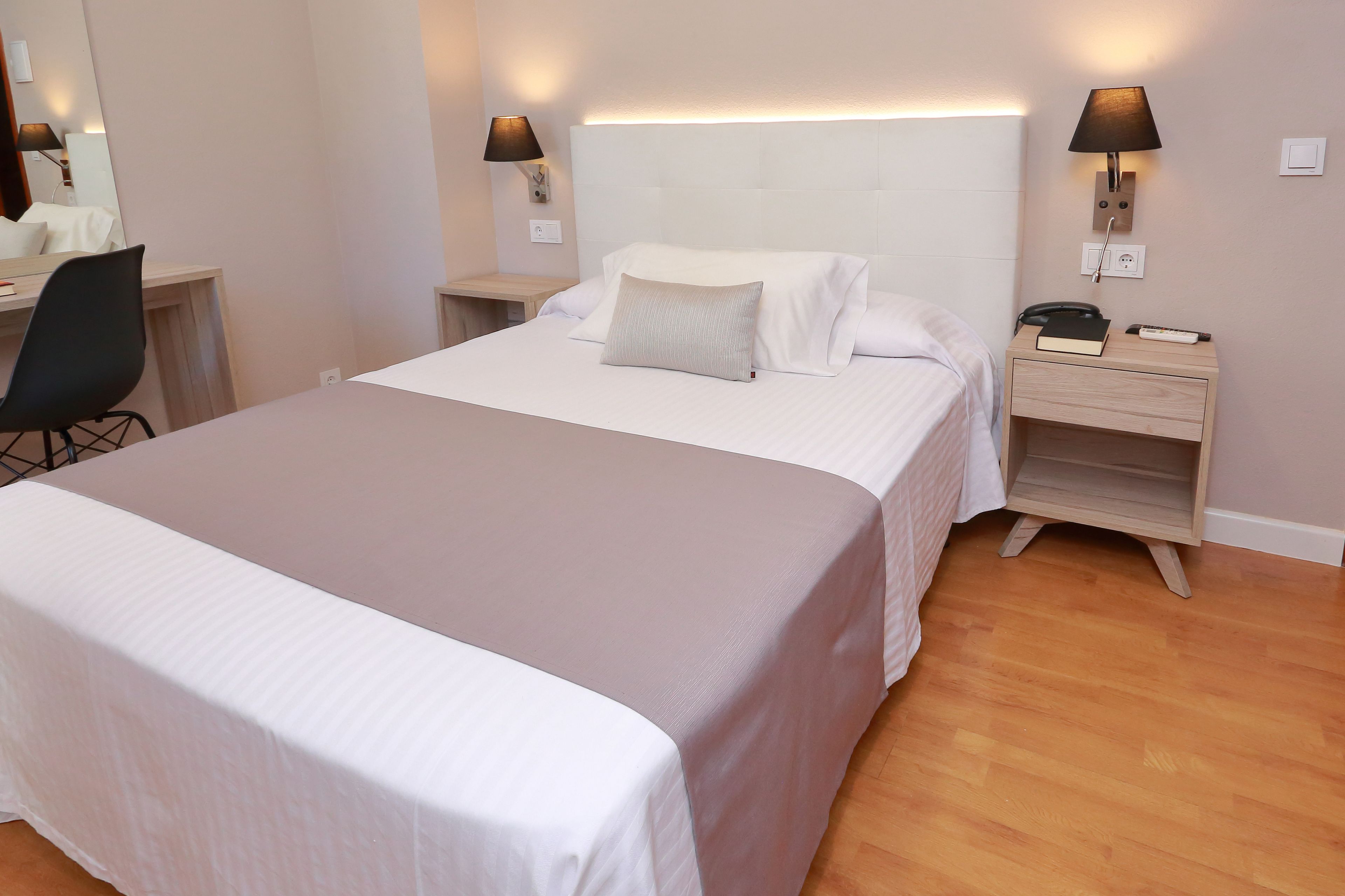 A neatly made bed with a white and grey duvet, a bedside table with a lamp, a book, and a phone.
