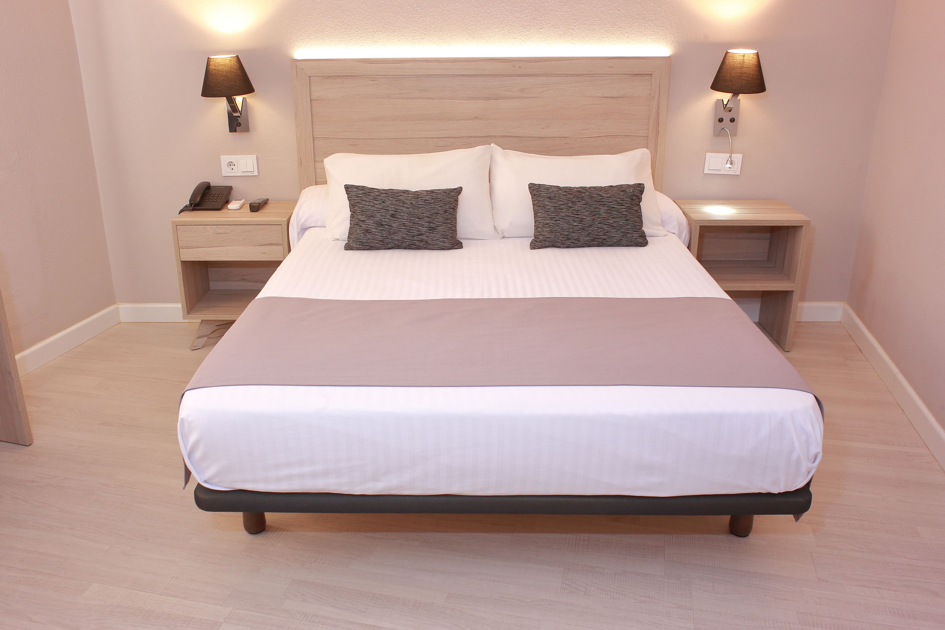 Cama bem arrumada com cabeceira de madeira, duas mesas de cabeceira com abajures e um telefone na mesa da esquerda.