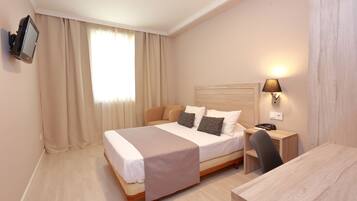 Una habitación de hotel con cama, mesita de noche, lámpara y televisor montado en la pared.