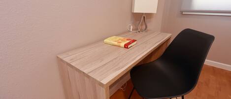 Un espacio de trabajo pequeño y ordenado con un escritorio de madera, una silla negra, una lámpara y un libro.