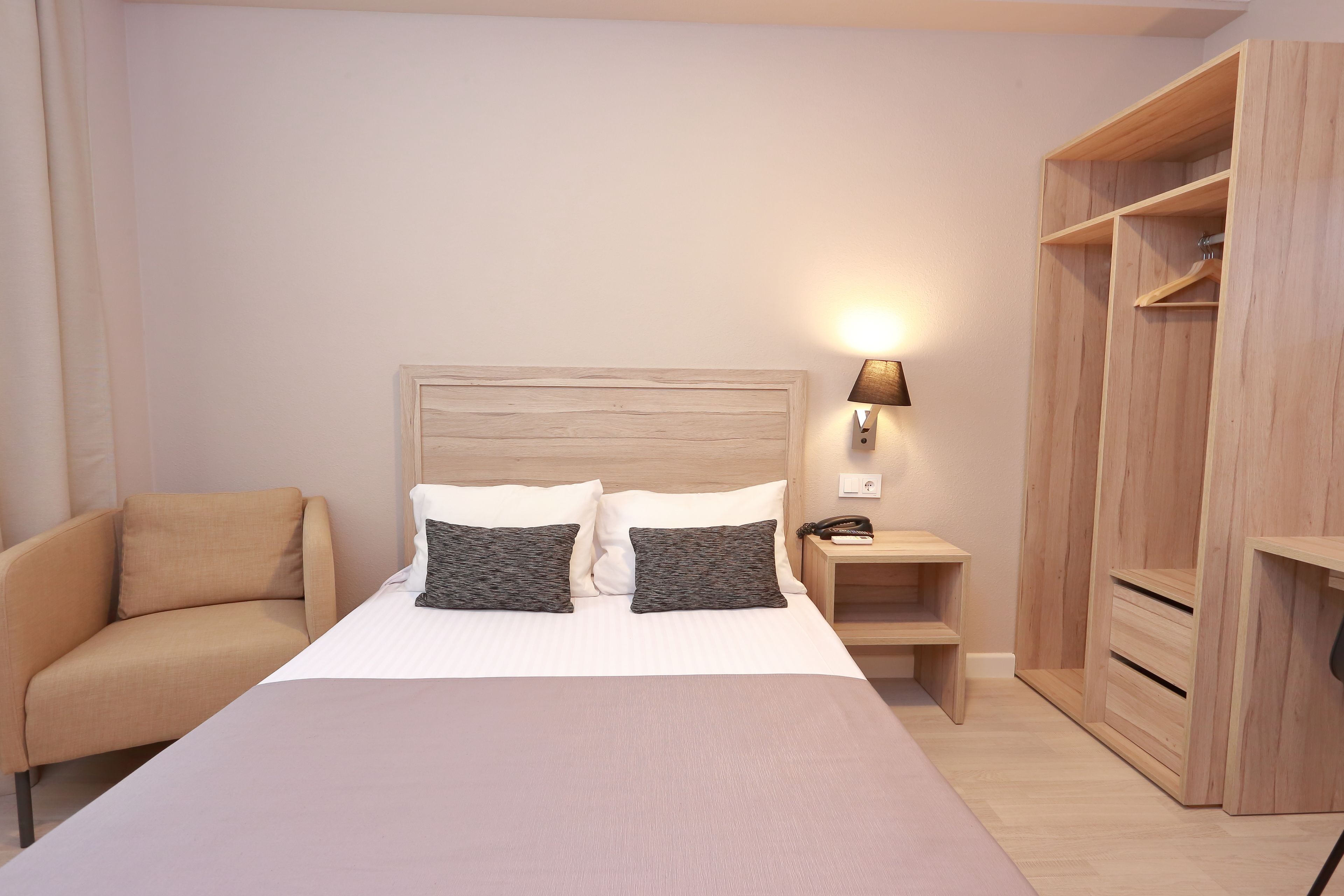 Una habitación de hotel ordenada con cama, una silla, una mesita de noche y un armario.