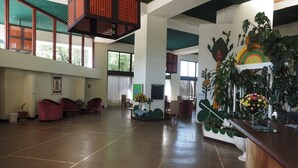 Um hall amplo com teto alto, grandes janelas e um balcão de recepção decorado com plantas.