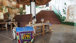 Quarto com sofá, mesa de madeira com tampo de vidro e escada com corrimão verde.