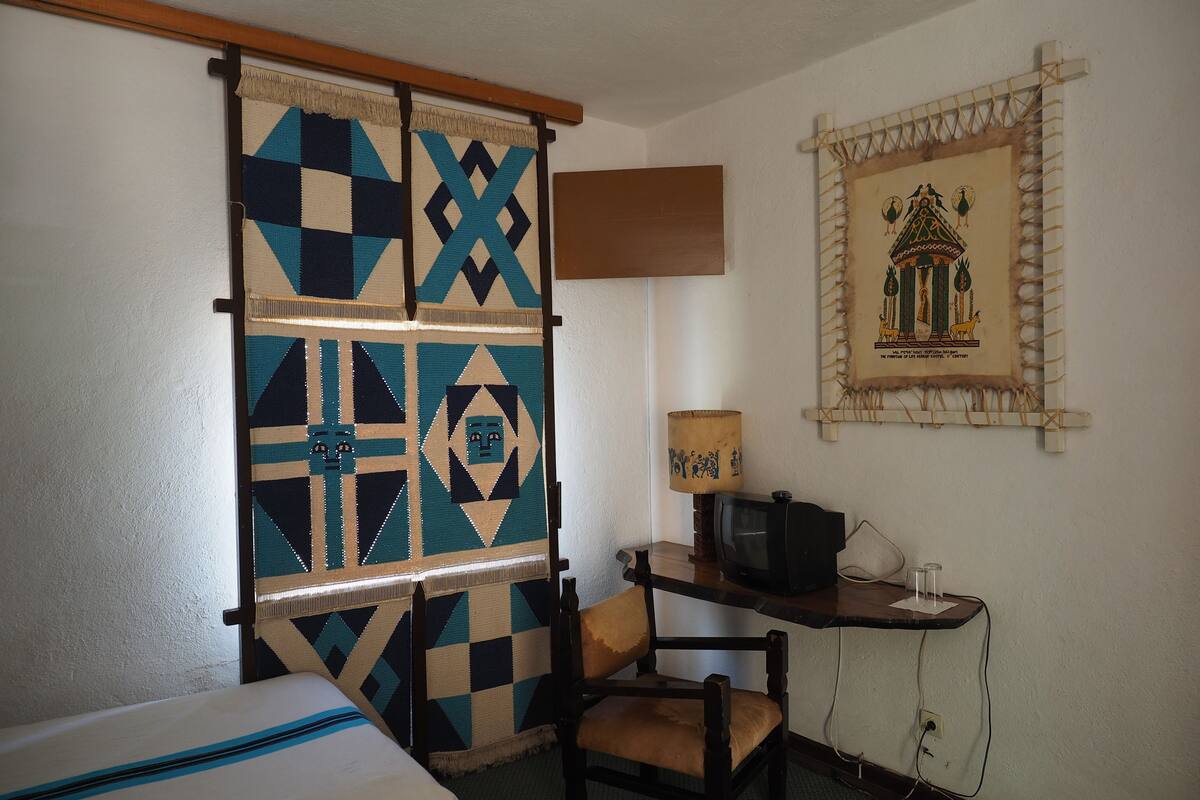 A room with a bed, a chair, a desk with a lamp, and a framed picture on the wall.
