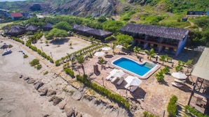 Vista aérea de un resort con piscina, playa y edificios de techo de paja.