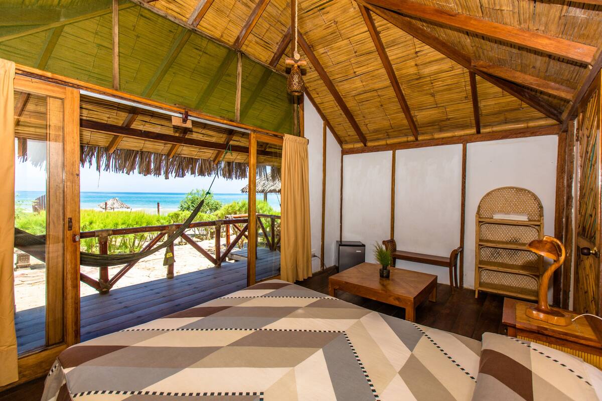 Una habitación con una cama grande, una mesa de madera, una silla y vista a la playa.