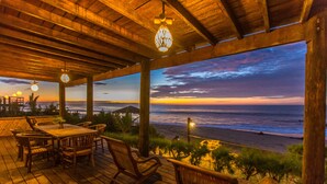 Terraza de madera con mesa y sillas con vista al océano al atardecer.