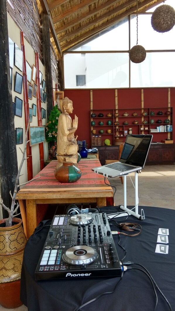 A room with a wooden Buddha statue, a laptop, a Pioneer DJ controller, and a collection of pottery on shelves.